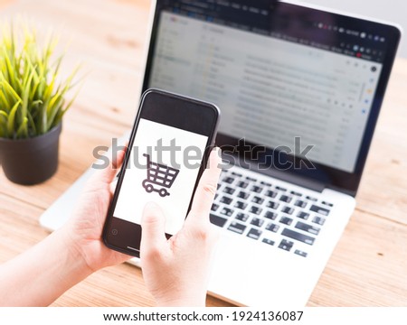 Online Shopping Website on Laptop. Shop by Smartphone, iPhone, iPad and Laptop. Close up Hands Using Smartphone Shopping Cart.