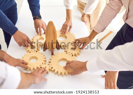 Business concept. Team of cropped company employees join gearwheels around toy rocket as metaphor for unity, teamwork, choosing new effective strategy and launching new project Royalty-Free Stock Photo #1924138553