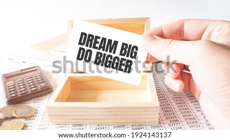 Businessman hold white card with text DREAM BIG DO BIGGER Calculator,wood box,money and financial documents