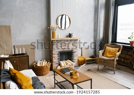 A coffee table by the fireplace of a country house and a wicker chair in the living room of the house in the Scandinavian style Royalty-Free Stock Photo #1924157285