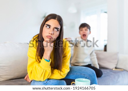 Kid anoying and disturbing exhausted and irritated mother in casual clothes holding hands on head while working at home