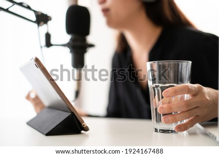 Unrecognizable Asian young woman relaxing and drinking water while live steaming a podcast, woman drinking water in a glass. Asian girl make a broadcasting via online radio or podcast.