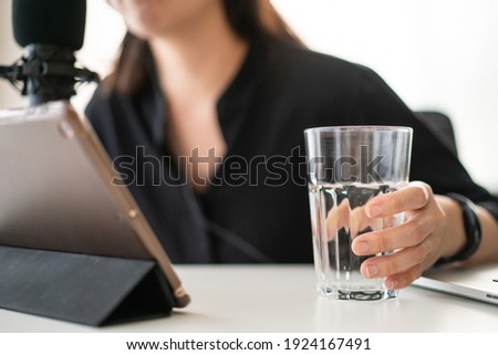 Unrecognizable Asian young woman relaxing and drinking water while live steaming a podcast, woman drinking water in a glass. Asian girl make a broadcasting via online radio or podcast.