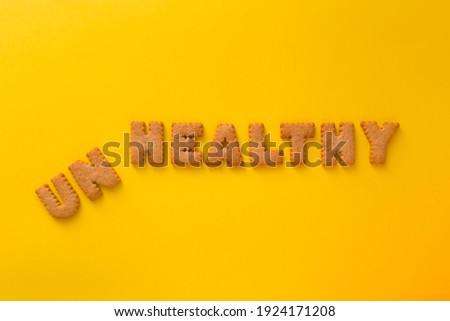 Word UnHealthy in the middle of the picture made of tasty crunchy cookies in form of big English alphabet letters, textured bright yellow background, health, dieting and medical concept. Copy space