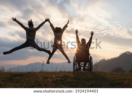 Silhouette Disabled handicapped woman in wheelchair with raised arms and children jumping at sunset. happy family concepts.