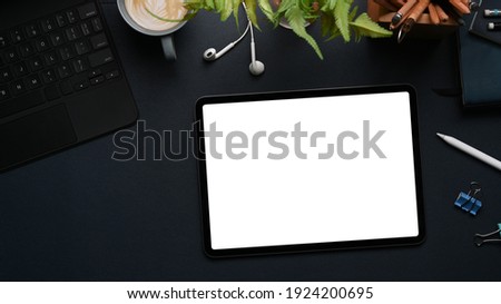 Top view of mockup digital table with empty screen, earphone, keyboard and plant on black background.