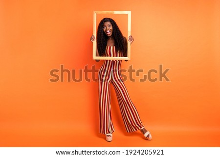 Full length photo of dark skin happy amazed woman hold wooden frame picture isolated on orange color background