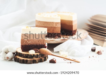 Three layered chocolate mousse cake on the wooden stand on white background. Good morning with fresh coffee and chocolate souffle cake. Vintage background
