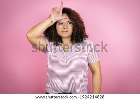 Young african american woman wearing red stripes t-shirt over pink background making fun of people with fingers on forehead doing loser gesture mocking and insulting.
