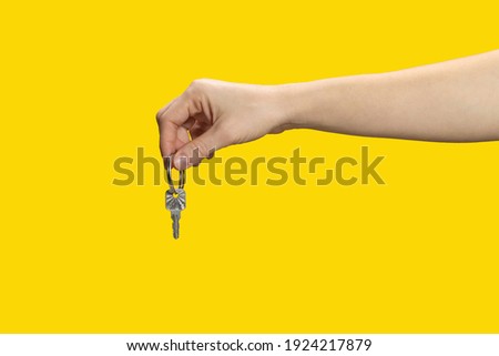 Female hand holding and giving house key on yellow background. Real estate agent.