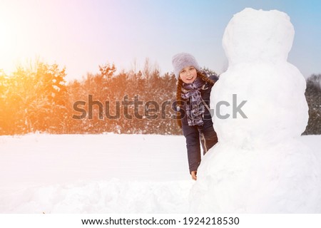 Cute girl makes a snowman on a winter day. A girl on a snow-covered field in the open air. Artistically colored and tinted photography