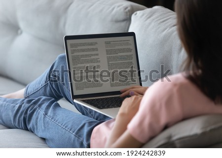 Rear shot of female study report translate text from foreign language using pc app. Young woman hold laptop on knees read electronic book work with document online. Focus on computer screen. Close up