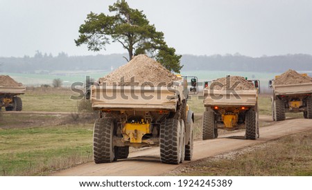 four yellow Volvo A40E and A40F articulated dump truck earth movers each fully laden with 25 tonne payload kick up clouds of dust as they convoy across Salisbury Plain, Wiltshire UK Royalty-Free Stock Photo #1924245389