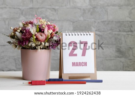 march 27. 27-th day of the month, calendar date.A delicate bouquet of flowers in a pink vase, two pencils and a calendar with a date for the day on a wooden surface..