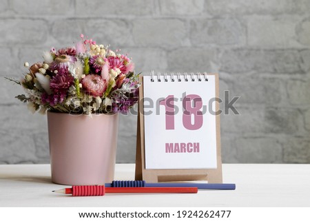 march 18. 18-th day of the month, calendar date.A delicate bouquet of flowers in a pink vase, two pencils and a calendar with a date for the day on a wooden surface..