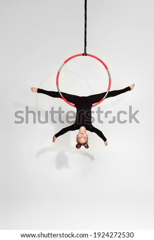 Little acrobat girl in black sportwear doing twine on an aerial hoop