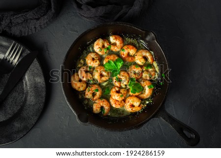 Shrimps with garlic, olive oil and parsley in frypan on black background