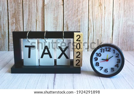 2022 number on wooden block cube and tax text on paper stand frame with black alarm clock on wooden background. Tax time concept Royalty-Free Stock Photo #1924291898