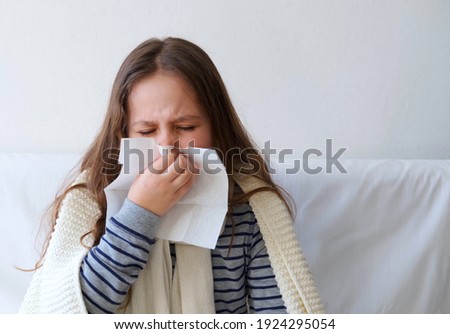 Ill cute elementary school girl with paper napkin blowing nose Royalty-Free Stock Photo #1924295054