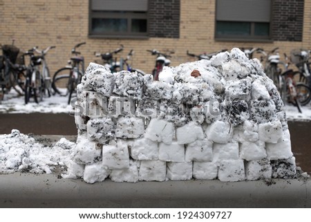 A brick wall made of dirty snow gathered at the street with nobody behind. Outdoor leisure activities to do with children. Stock photography.