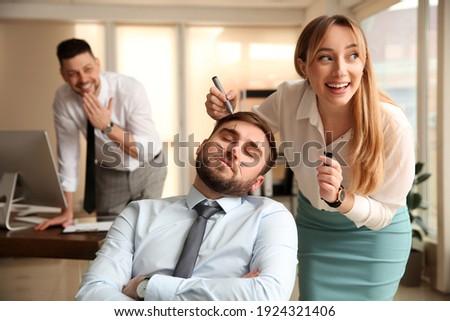 Young woman drawing on colleague's face while he sleeping in office. Funny joke Royalty-Free Stock Photo #1924321406