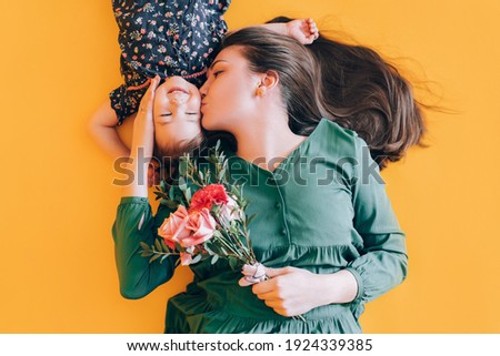 Mom and daughter are playing on a yellow background. Child gives mom flowers for a holiday.