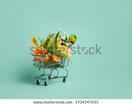 Flowers in miniature shopping trolley on pastel turquoise background. Flower delivery concept with copy space. Sale, shopping for the holidays, Mothers Day, Women's Day, Valentines Day or Birthday.