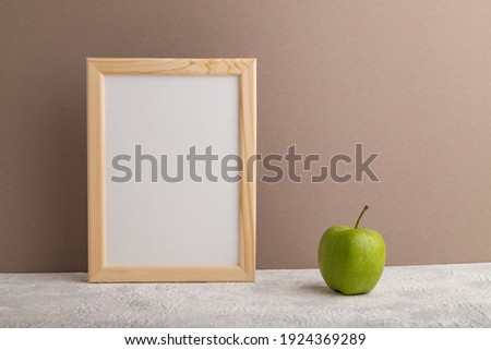 White wooden frame mockup with green apple on beige paper background. Blank, vertical orientation, still life, copy space.