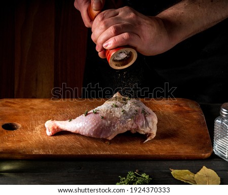 Cooking a chicken leg with the hands of a chef on a dark background. Add pepper to chicken meat. Free advertising space for a restaurant