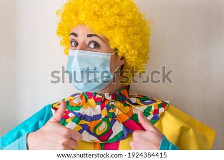 Young woman dressed in a clown costume wearing a disposable mask and a yellow clown wig doing the ok sign with her hands. Protection from sars-cov-2 virus 