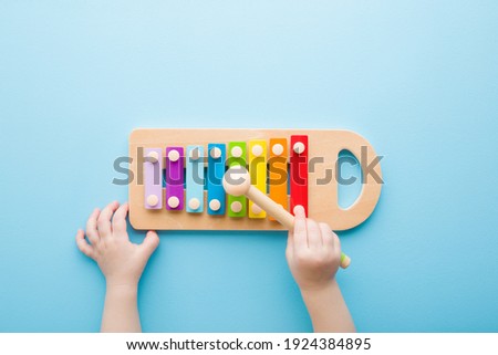 Baby hand holding hammer and playing colorful xylophone on light blue table background. Closeup. Music toy instrument of development for little kids. Point of view shot.