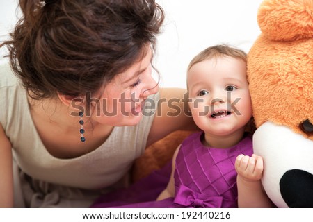 Mother and dauhter are laughing while playing with teddy bear
