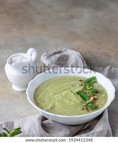 Vegetarian cream soup of green vegetables (broccoli, green peas, spinach) served with mint and seeds on concrete background. Clean eating, healthy food concept. Selective focus.