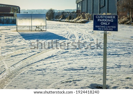 customer parking only sign post over empty parking space covered with winter snow in england uk.