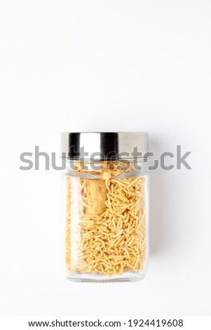 Indian spicy snacks (Namkeen) - Bikaneri Besan Bhujia in a glass jar with a closed lid, made with chickpea flour (Besan), Top view, over the white background.