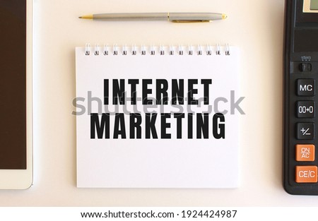 Notepad with text INTERNET MARKETING on a white background, near calculator, tablet and pen.
