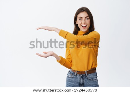 Look at this big thing. Excited smiling woman showing big object with hands on empty space, shaping box, sanding against white background. Royalty-Free Stock Photo #1924450598