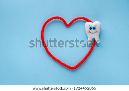 White felt tooth with red heart on blue background. Dental health concept. World dentist day concept. Flat lay, top view, copy space.