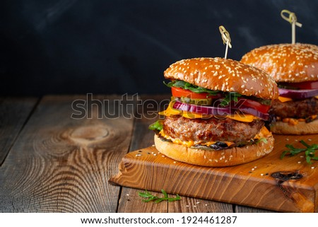 Two delicious homemade burgers of beef, cheese and vegetables on an old wooden table. Fat unhealthy food close-up. With copy space.