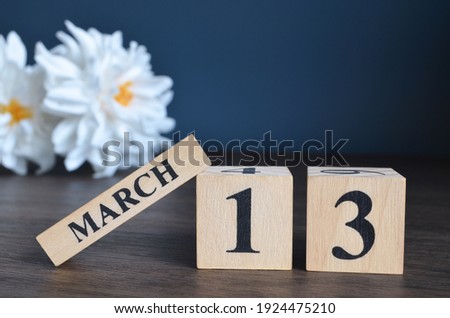 March 13, Date cover design with calendar cube and white Paeonia flower on wooden table and blue background.