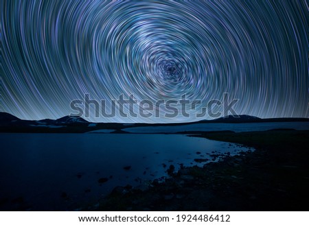Beautiful small lake and mountains under the colorful star trails on the sky. Night time lapse photography.v
