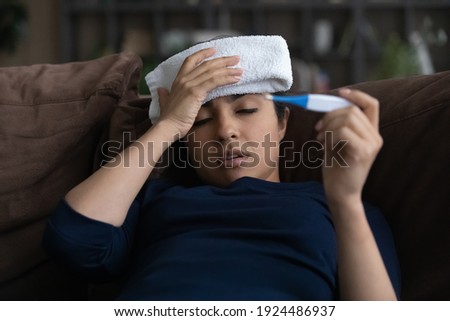 Unhealthy millennial Indian woman struggle with high temperature measure with thermometer. Sick ill young ethnic female suffer from flu or cold, have covid-19 lying at home. Corona virus concept. Royalty-Free Stock Photo #1924486937