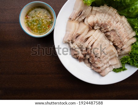 picture view top corner boiled pork belly, turned intopiece just right to eat into mouth On white plate And spicy sauce On the brown wood floor It is popular food among Thai and Chinese people.