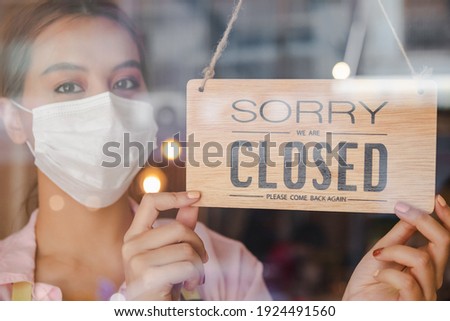 Young Asian owner retail, coffee shop woman turning signboard to closed with wearing face mask, protection to pandemic of coronavirus.Close store,restaurant or pub due to lockdown, quarantine of covid.
