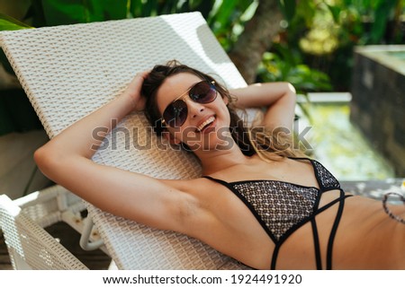 On the shisong by the pool lies a girl in a swimsuit with a charming smile in dark glasses. High quality photo