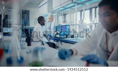 Modern Medical Research Laboratory: Two Scientists Use Computer with Screen Showing DNA Gene Analysis, Specialists Discuss Innovative Technology. Advanced Scientific Lab for Medicine, Biotechnology
