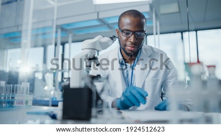 Modern Medical Research Laboratory: Portrait of Male Scientist Using Microscope, Writing Down Analysis Information. Advanced Scientific Lab for Medicine, Biotechnology, Microbiology Development Royalty-Free Stock Photo #1924512623