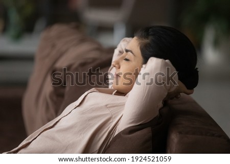 Calm young Indian woman relax on couch at home sleep or take nap relieving negative emotions. Relaxed happy millennial mixed race female rest on sofa daydream or doze. Peace, stress free concept. Royalty-Free Stock Photo #1924521059