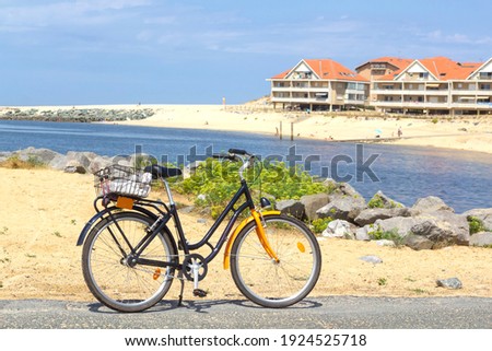 Orange bicycle with the beautiful Landes scenery on the foreground : blue sea, sandy beach and vacation rental houses with typical orange tiled roofs on the West Coast of France. 