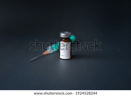 A vial of coronavirus vaccine, a syringe with a needle, with a black background.
